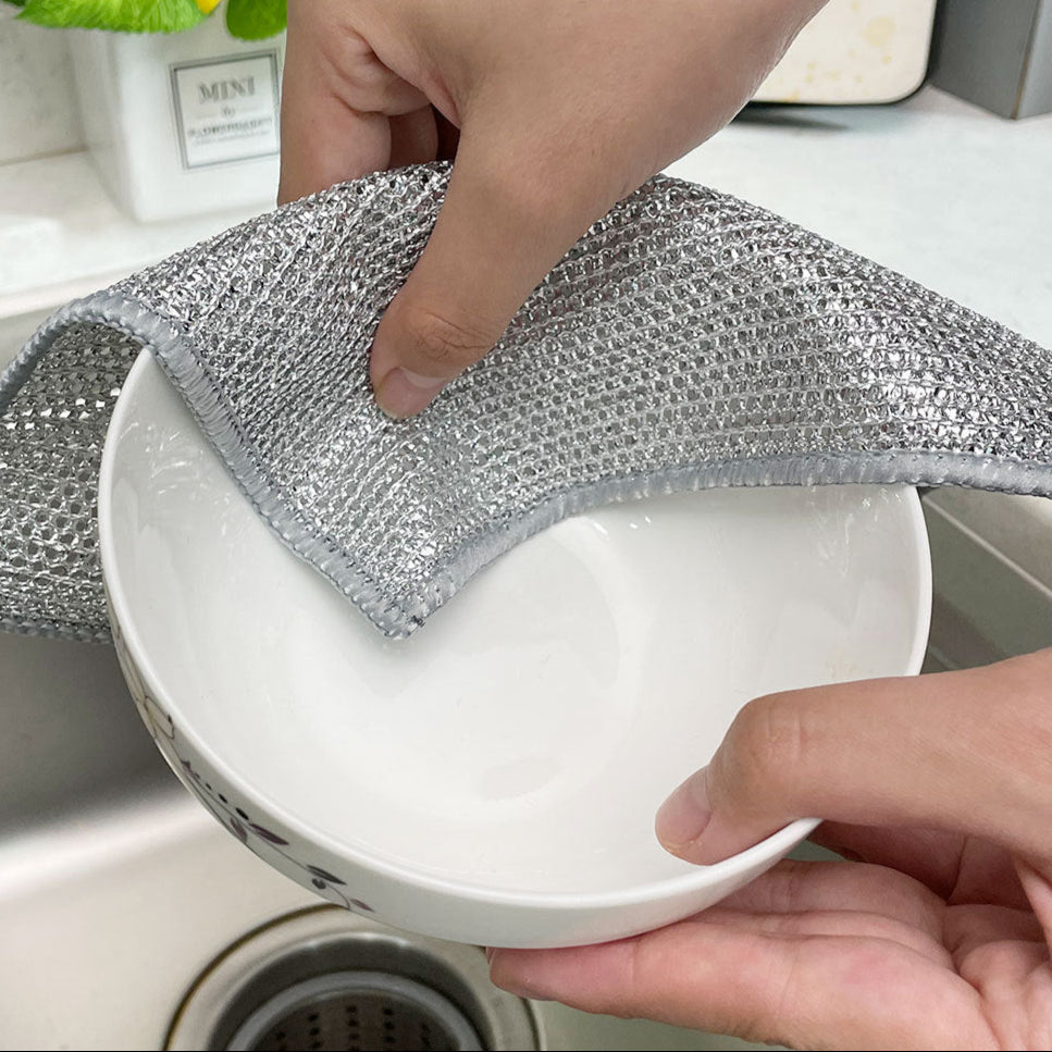 Person cleaning a white bowl with a metallic scrubber in a kitchen setting.