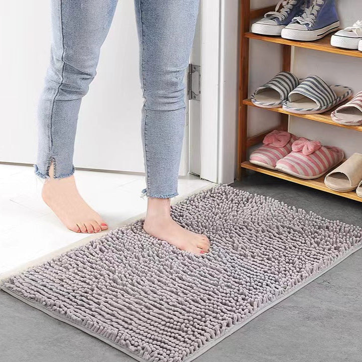 A person stepping onto a gray Super Absorbent Door Mat with shoes and slippers on a shelf in the background.
